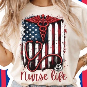 May include: A cream-coloured t-shirt with a distressed American flag design, a red caduceus, and a stethoscope. The words "Nurse Life" are written in a cursive font below the graphic. The design incorporates red, white, and blue colours.