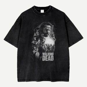 Puede incluir: Camiseta negra con un gráfico en escala de grises de personajes de la serie "The Walking Dead". El diseño incluye retratos de varios personajes y el título del programa en una fuente desgastada. La camiseta tiene un aspecto vintage.
