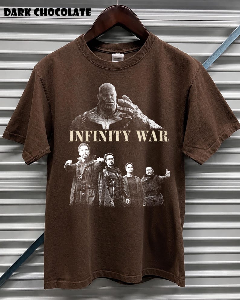 K&ouml;nnte beinhalten: Dunkel schokoladenbraunes T-Shirt mit einer Grafik aus dem Film "Infinity War". Das Design zeigt Thanos und andere Charaktere. Der Text "DARK CHOCOLATE" steht oben. Das T-Shirt h&auml;ngt an einem Holzkleiderb&uuml;gel.