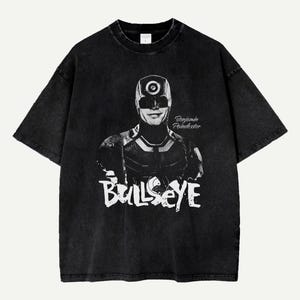 Puede incluir: Camiseta negra con un gráfico que representa a Bullseye, un personaje de cómic. El diseño incluye un retrato del personaje con la palabra "Bullseye" en letras blancas. La camiseta también tiene el texto "Benjamin Poindexter".