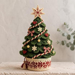 May include: A crocheted Christmas tree in dark green with a cream-colored base featuring a red snowflake pattern. The tree is decorated with small red hearts, white snowflakes, yellow spheres, red and white gingham bows, and a cream star topper.