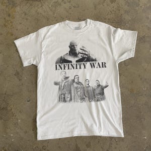 K&ouml;nnte beinhalten: Wei&szlig;es T-Shirt mit einer Schwarz-Wei&szlig;-Grafik von Thanos und anderen Charakteren aus dem Film "Infinity War". Der Text "INFINITY WAR" ist &uuml;ber den Charakteren aufgedruckt. Das Shirt hat einen Rundhalsausschnitt und kurze &Auml;rmel.