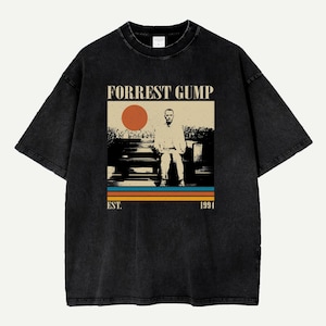 May include: Black t-shirt featuring a graphic from the movie "Forrest Gump." The design includes the film's title, a seated figure, and a retro color scheme with an orange sun and horizontal stripes. The text "EST. 1994" is also included.