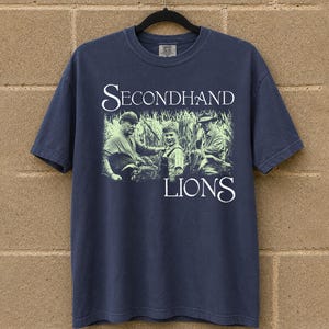 May include: Navy blue t-shirt featuring a graphic from the movie "Secondhand Lions." The design includes a black and white image of three people in a field, with the movie title in white script.
