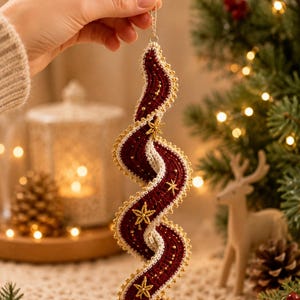 May include: A spiral-shaped Christmas ornament featuring deep burgundy crochet fabric with a cream-colored border. The ornament is embellished with small gold beads along the edges and embroidered gold star motifs on the burgundy surface.