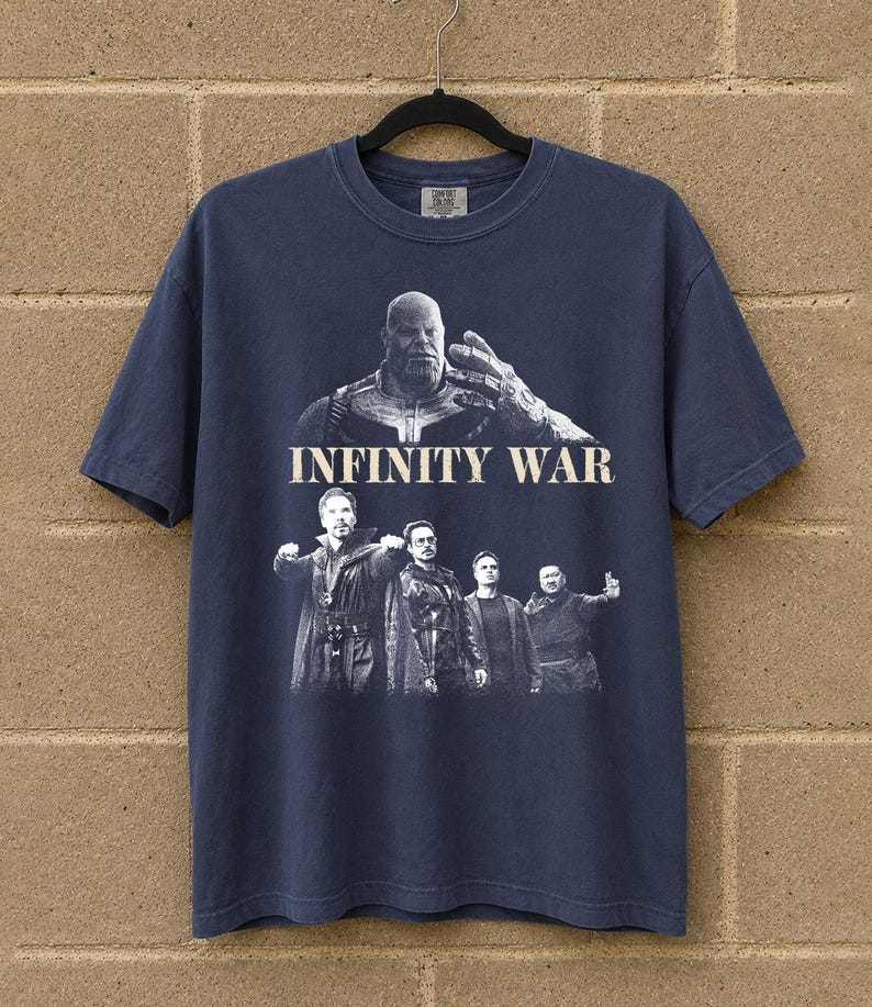 K&ouml;nnte beinhalten: Marineblaues T-Shirt mit einer Grafik aus dem Film "Infinity War". Das Design zeigt den Text "INFINITY WAR" &uuml;ber einer Darstellung von Thanos und anderen Charakteren. Das T-Shirt h&auml;ngt an einem schwarzen Kleiderb&uuml;gel.