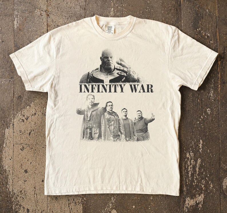 K&ouml;nnte beinhalten: Cremefarbenes T-Shirt mit einer Grafik von Thanos und anderen Charakteren aus dem Film "Infinity War". Der Text "INFINITY WAR" ist in fetten, schwarzen Buchstaben unter dem Thanos-Bild aufgedruckt. Das Shirt hat einen Rundhalsausschnitt und kurze &Auml;rmel.