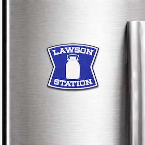 May include: A blue and white Lawson Station magnet. The magnet has a blue shield shape with the words "LAWSON" and "STATION" in white. A white milk bottle graphic is in the center.