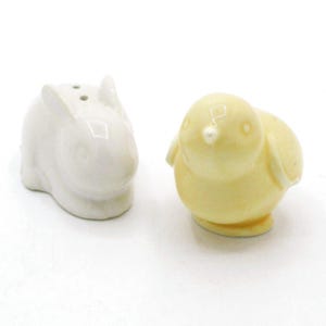 May include: A ceramic salt and pepper shaker set featuring a white bunny and a yellow chick. The bunny has two holes on top, and the chick has a small beak. The set is designed for the kitchen and adds a touch of spring.