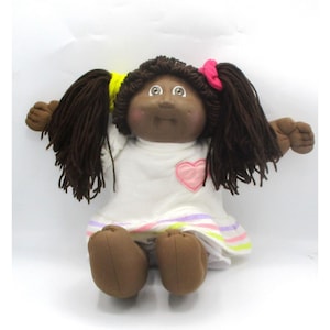 Muñeca Cabbage Patch Kids afroamericana de 1985 con vestido blanco, cabello de lana marrón y certificado de nacimiento.