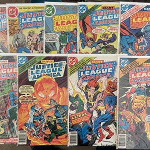 May include: A collection of vintage "Justice League of America" comic books. The covers feature vibrant illustrations of superheroes in action, with bold text and the DC Comics logo. The comics are in protective sleeves.