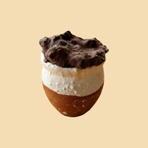 May include: A small, rounded ceramic vessel with a terracotta-colored base, a white textured middle section, and a dark brown, uneven, craggy top layer. The letters CT are faintly embossed on the lower terracotta portion of the container.