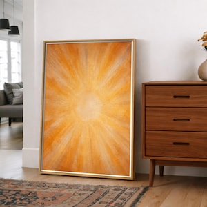 May include: A rectangular framed wall art piece featuring an abstract sunburst design in shades of warm orange, gold, and yellow. The artwork displays radiating brushstrokes that emanate from a central point, encased in a thin metallic frame.
