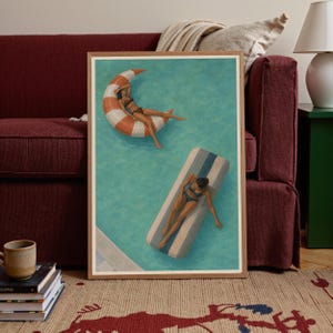 May include: A framed art print depicting two individuals in swimsuits floating in a turquoise swimming pool. One person rests on a crescent-shaped orange and white striped float, while the other lies on a rectangular blue and white striped float.
