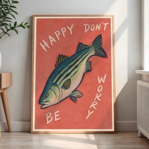 Può includere: Una stampa artistica da parete rettangolare con un'illustrazione stilizzata di un branzino striato centrata su uno sfondo rosso corallo. Il testo "HAPPY DON'T BE WORRY" è stampato in bianco con un carattere scritto a mano attorno al pesce.