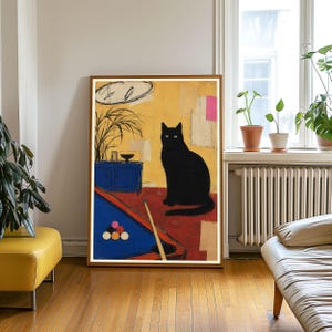 May include: A framed art print featuring a black cat sitting on a red floor next to a blue pool table with a rack of billiard balls and a cue stick. The background is yellow with a blue cabinet, a plant, and abstract shapes in pink and white.