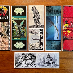 May include: A set of 7 bookmarks featuring illustrations of mythical creatures and cryptids. The bookmarks are printed on cardstock and have a glossy finish. The illustrations include Bigfoot, Mothman, the Jersey Devil, Nessie, and the Abominable Snowman. The bookmarks are all different colors and have a vintage aesthetic.