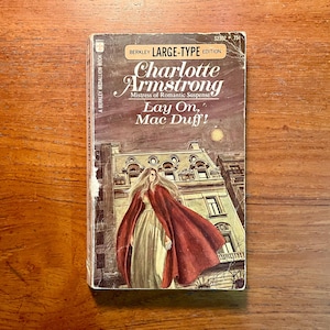 May include: A vintage paperback book titled "Lay On, Mac Duff!" by Charlotte Armstrong. The cover features a woman in a red cloak in front of a building. The book is a Berkley Medallion Book, large-type edition.