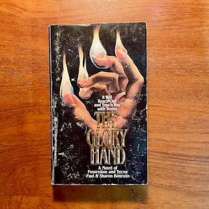 May include: A paperback book titled "The Glory Hand" with a dark cover featuring a hand with long, sharp nails. The book's title is in gold lettering, and the cover includes the text "It Will Reach Out and Touch You with Terror."