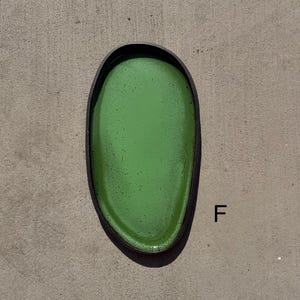 May include: An oval-shaped tray with a vibrant green interior surface featuring subtle dark speckles and a contrasting dark, textured outer rim. The letter F is printed in black to the right of the tray, which has a smooth, glossy finish.