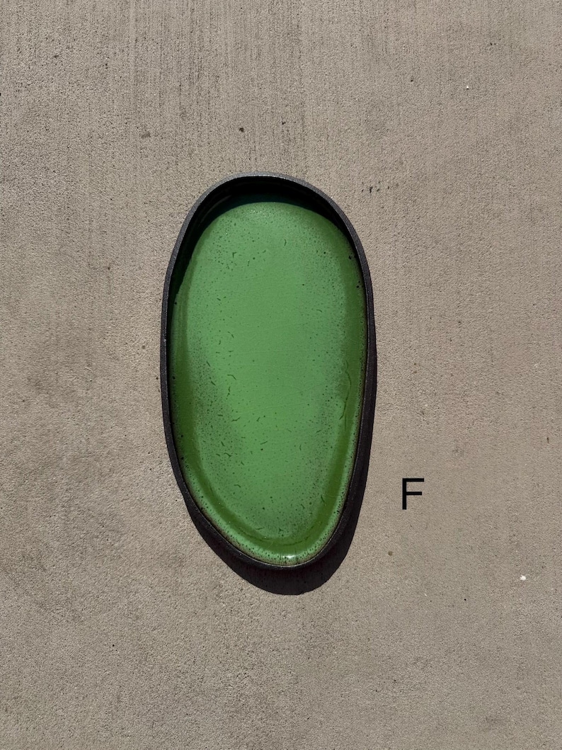May include: An oval-shaped tray with a vibrant green interior surface featuring subtle dark speckles and a contrasting dark, textured outer rim. The letter F is printed in black to the right of the tray, which has a smooth, glossy finish.