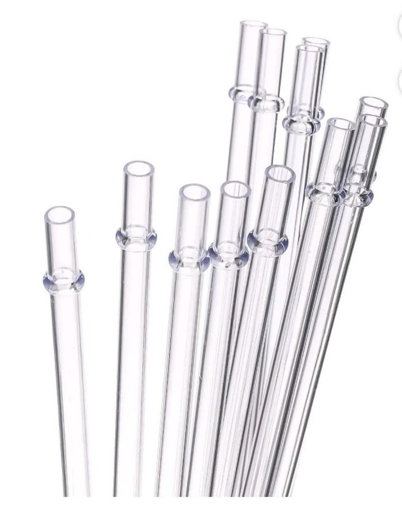 May include: A collection of clear glass straws, each with a slightly flared top and a small ring detail near the top. The straws are arranged at various angles against a white background, showcasing their transparency and simple design.