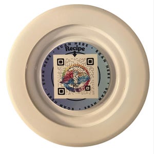 May include: A white, circular object with a central, circular design. The design features a QR code and the words "SCAN HERE Recipe". The design has a colorful, abstract pattern. The object is set against a white background.