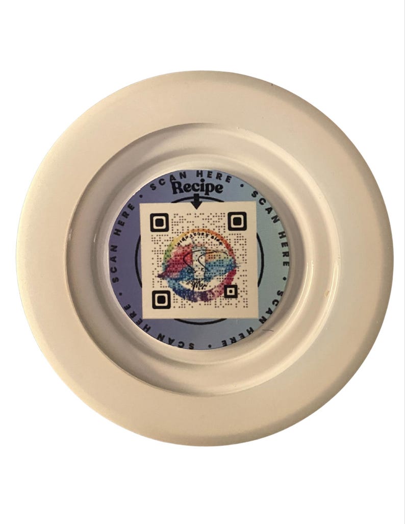 May include: A white, circular object with a central, circular design. The design features a QR code and the words "SCAN HERE Recipe". The design has a colorful, abstract pattern. The object is set against a white background.