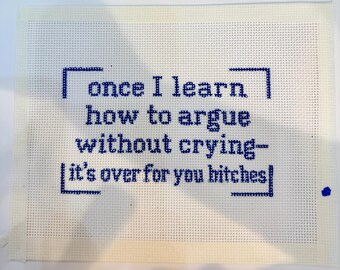 May include: A rectangular piece of white needlepoint canvas featuring dark blue cross-stitched text that reads: once I learn how to argue without crying- it's over for you bitches. The text is framed by four blue corner brackets.