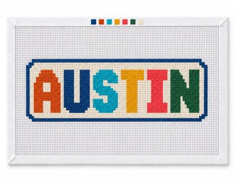 Könnte beinhalten: Eine rechteckige Stickleinwand mit dem Wort AUSTIN in großen, mehrfarbigen Blockbuchstaben. Die Buchstaben sind orange, dunkelblau, hellblau, gelb, rot und grün und dunkelblau umrandet. Oben befindet sich ein Streifen mit der Farbpalette.