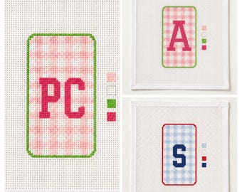 Könnte beinhalten: Drei quadratische weiße Stickleinen mit mittigen rechteckigen Aufnähern im Vichy-Karo-Muster. Ein Aufnäher zeigt die Buchstaben PC in Pink, einer den Buchstaben A in Pink und einer den Buchstaben S in Marineblau, jeweils mit kleinen Farbmustern.