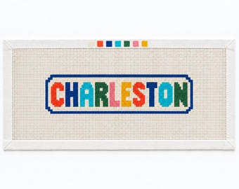 Könnte beinhalten: Eine rechteckige Stickleinwand mit dem Wort CHARLESTON in mehrfarbigen Blockbuchstaben, darunter Rot, Blau, Grün, Pink und Gelb. Der Text ist von einem blauen Rahmen umgeben, mit einer Reihe kleiner farbiger Quadrate in der oberen Mitte.