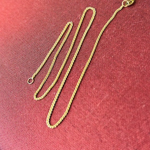 May include: Three gold chains of different lengths, all with a delicate, braided design. The chains are laid out on a red fabric background.