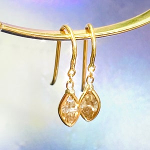 May include: A pair of gold dangle earrings with teardrop-shaped clear stones.