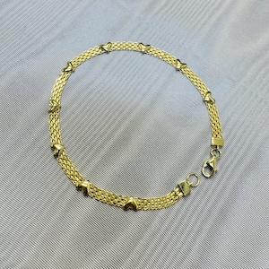 May include: A gold-toned bracelet featuring a woven mesh chain design accented with small, evenly spaced heart-shaped charms. The bracelet includes a secure lobster claw clasp and a small circular jump ring at the end for fastening.