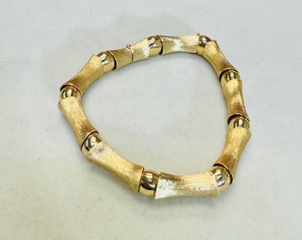May include: A gold bamboo-style bracelet with a brushed finish. The bracelet is made of linked, round, and oval-shaped pieces.