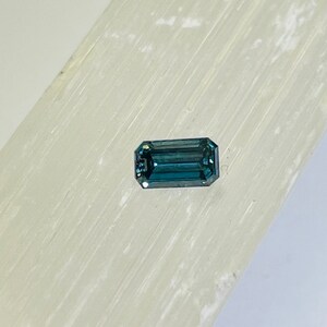 May include: A dark blue, emerald-cut gemstone on a white background.
