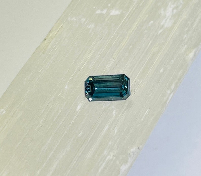 May include: A dark blue, emerald-cut gemstone on a white background.