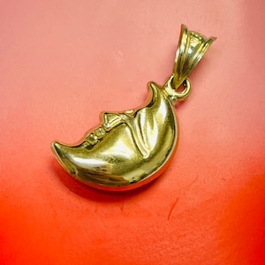 May include: A gold crescent moon pendant charm. The moon is detailed with a face and a textured surface.