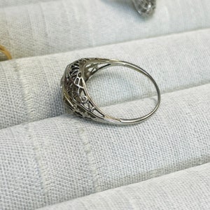 May include: A delicate silver ring with a filigree design and a small round gemstone in the center.