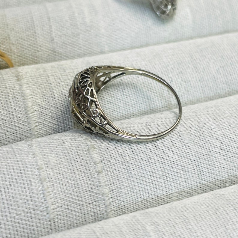 May include: A delicate silver ring with a filigree design and a small round gemstone in the center.