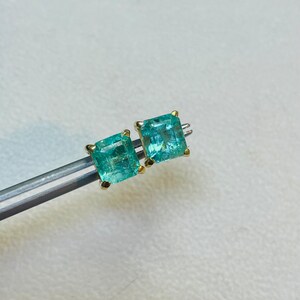 May include: A pair of emerald green gemstone earrings with gold settings. The earrings are square shaped and have a faceted cut.