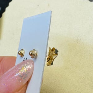 Op de afbeelding: Goudkleurige oorstekers met een textuurontwerp. De oorbellen worden gepresenteerd op een witte kaart, met de nadruk op de ingewikkelde details van de sieraden. De oorbellen zijn klein en delicaat, geschikt voor dagelijks gebruik.
