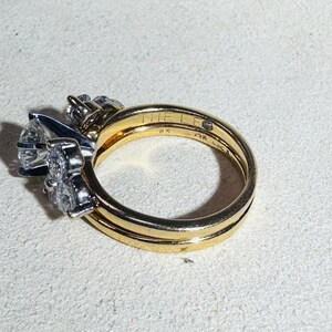 May include: A set of gold rings with a diamond cluster and a solitaire diamond ring. The gold band has the text "MIE LEE" and "85" engraved on it. The rings are set on a white surface.