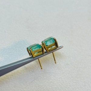 May include: A pair of gold earrings with light blue square-shaped gemstones.