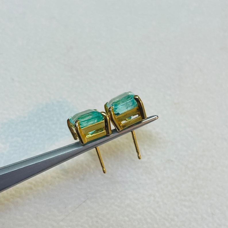 May include: A pair of gold earrings with light blue square-shaped gemstones.