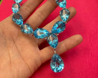 May include: A delicate necklace with a teardrop pendant, both featuring large, faceted, sky blue topaz stones. The necklace is made of white metal and has a simple, elegant design.