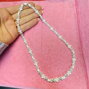 May include: A silver necklace with a twisted chain design and small flower accents.