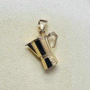 Könnte beinhalten: Ein goldfarbener Anhänger in Form eines Espressokochers. Der Anhänger hat oben eine Schlaufe für eine Kette und einen kleinen Griff an der Seite. Der Espressokocher ist etwa 2,5 cm hoch.