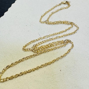 Op de afbeelding: Een goudkleurige ketting bestaande uit een reeks onderling verbonden, gedraaide ovale schakels. De ketting heeft een gepolijste, reflecterende afwerking en is voorzien van een kleine, veilige karabijnsluiting aan het uiteinde van de lus.